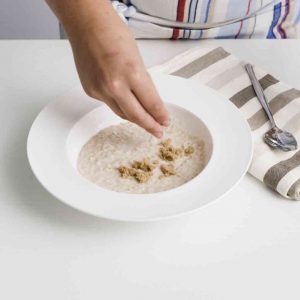 person-sprinkling-porridge-with-topping